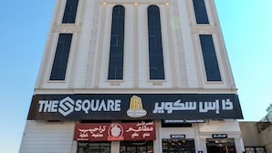Un hotel llamado "The Square" con una fachada moderna, múltiples ventanas y un estacionamiento con varios coches.