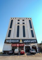 Un hôtel appelé « The Square », doté d’une façade moderne, de nombreuses fenêtres et d’un espace de réception.