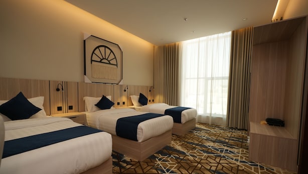 Habitación de hotel con dos camas, un ventanal con cortinas, una alfombra con estampado geométrico y una obra de arte colgada en la pared.