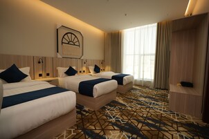 Une chambre d’hôtel avec deux lits, une grande fenêtre avec des rideaux, une moquette à motifs géométriques et une œuvre d’art accrochée au mur.