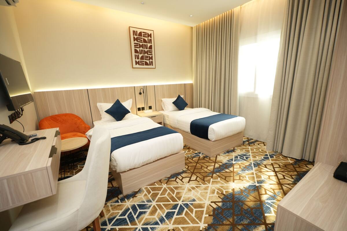 A hotel room with two beds, a desk, a chair, and a patterned floor.