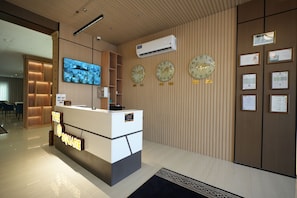 Een receptiebalie met een digitaal scherm, klokken, certificaten en een wandairconditioner.