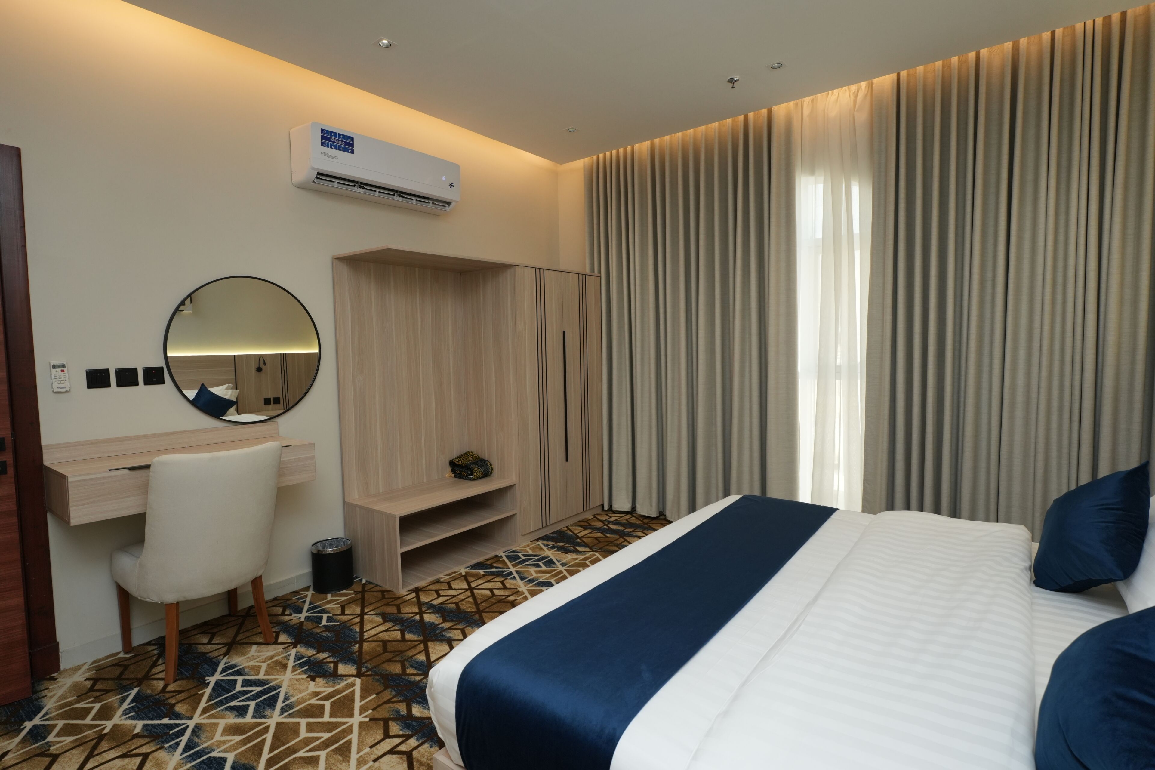 A hotel room with a bed, a desk, a chair, a wardrobe, and a large window with curtains.