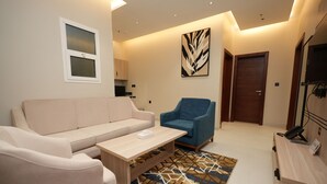 Una sala de estar moderna con un sofá color beige, un sillón azul, una mesa de centro de madera y una alfombra estampada.