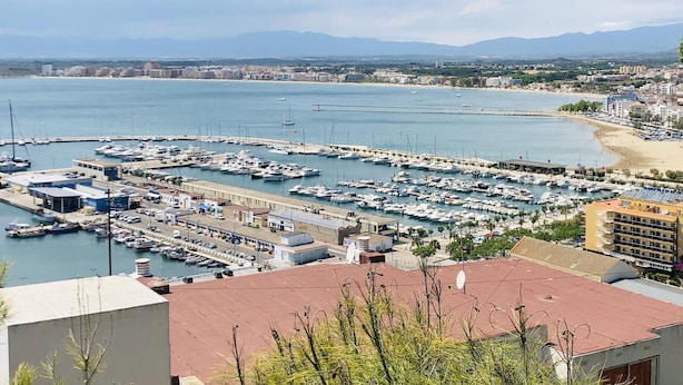 Un port de plaisance où sont amarrés de nombreux bateaux, une plage de sable et, en arrière-plan, une vue sur la ville.