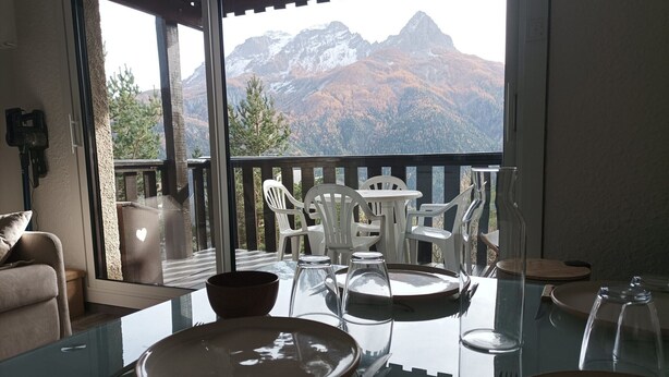 Un coin repas avec une table en verre, des chaises blanches et une vue sur les montagnes.