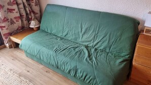 Un sofá verde en una habitación con suelo de madera, una mesita de madera y una lámpara.