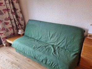 Vihreä sohva huoneessa, jossa on puulattia, pieni puupöytä ja lamppu.