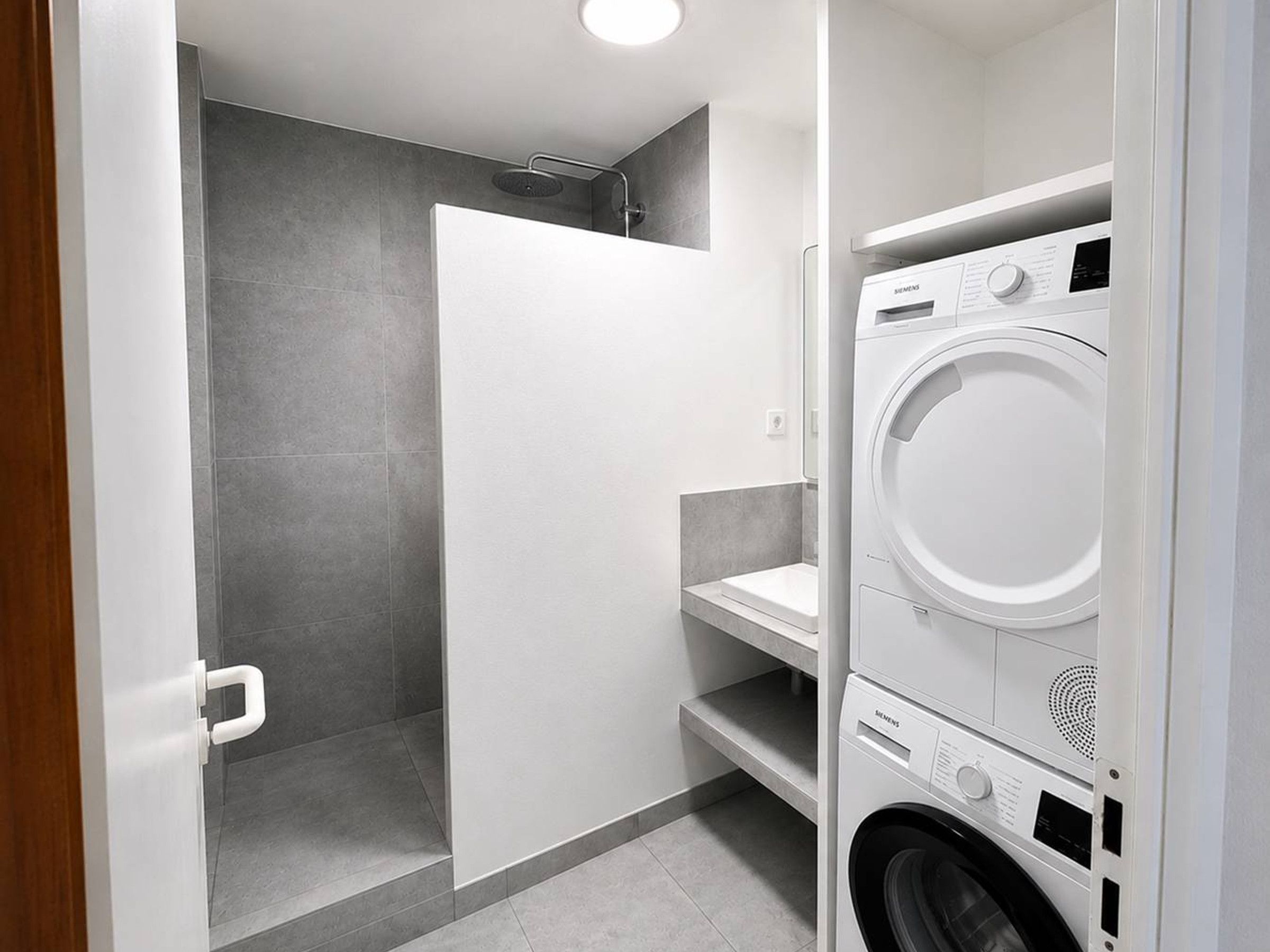 Een wasruimte met een wasmachine en droger, een doucheruimte en een witte deur.