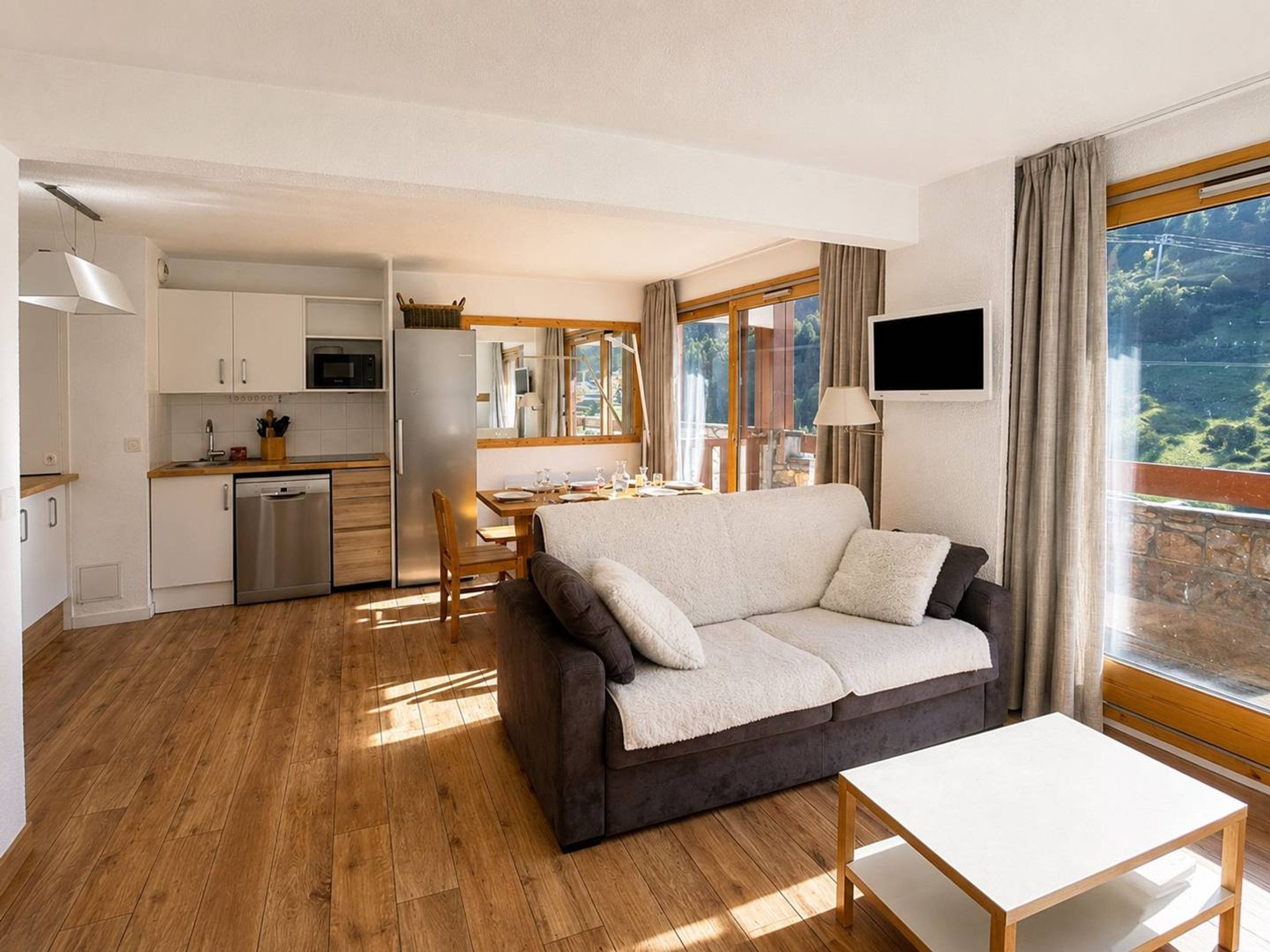 En moderne stue med sofa, spisebord og et køkkenområde med skabe og hårde hvidevarer.