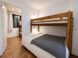 Dormitorio con literas, cabecero de madera, lámpara de noche y ventana con cortinas.