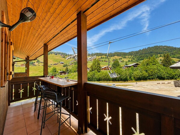 Un balcón de madera con vistas a un telesilla y colinas verdes.