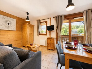 A cozy room with a wooden cabinet, a television on a stand, a dining table with chairs, and a window with curtains. - Cozy studio cabin at ski slopes, 4 pers, balcony (Notre-Dame-de-Bellecombe)