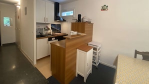 Et kompakt køkken med hvide skabe, en træbordplade, en sort emfang og et lille vindue.
