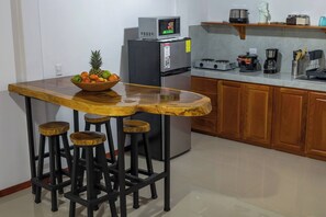 A kitchen with a wooden bar stool set, a refrigerator, a microwave, and a coffee maker. - Apartamento Lantanas (Parrita)