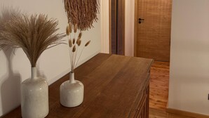 A wooden dining table with two white vases containing dried plants, a woven wall hanging, and a wooden door with a light fixture above it. - Idyllic holiday home with far-reaching views, fireplace and secluded location. (Buchenberg)