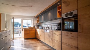 A modern kitchen with wooden cabinets, a built-in oven, and a large window providing natural light. - Idyllic holiday home with far-reaching views, fireplace and secluded location. (Buchenberg)