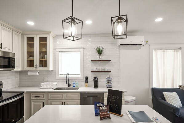 A modern kitchen with white cabinets, a built-in oven, a microwave, a dishwasher, and a large island with a chalkboard.