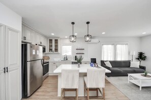 A modern kitchen with white cabinetry, a stainless steel refrigerator, and a dining area with a white table and chairs. - The Lockwood, Residence One | EaDo by the Stadiums (Houston)