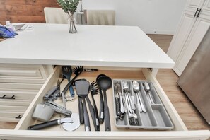 Un tiroir de cuisine contenant des ustensiles et un vase posé sur la table.
