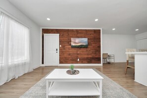 Un salon moderne avec une table basse blanche, un téléviseur fixé au mur et un mur d’accent en bois.