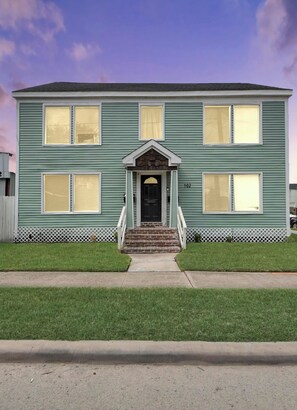 A two-story house with a front porch, a number '102' on the side, and a picket fence. - The Lockwood, Residence One | EaDo by the Stadiums (Houston)