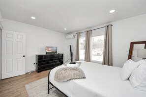 A bedroom with a bed, a dresser, a TV, and a window with curtains. - The Lockwood, Residence One | EaDo by the Stadiums (Houston)