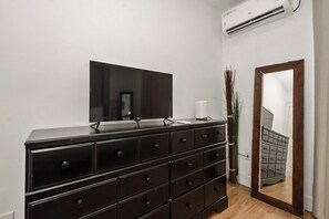 A bedroom with a black dresser, a flat-screen TV, a mirror, and an air conditioner on the wall.