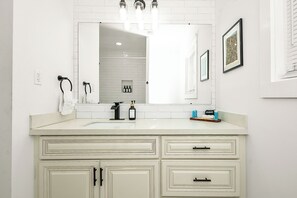 A bathroom with a white vanity, a mirror, and a framed picture on the wall.