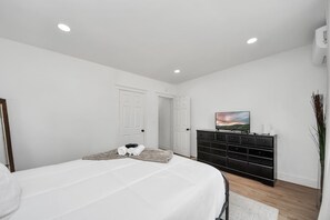 A bedroom with a bed, a dresser, a television, and a door. - The Lockwood, Residence One | EaDo by the Stadiums (Houston)