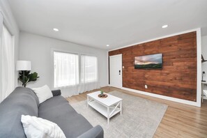 A modern living room with a grey sofa, white coffee table, and a wooden accent wall. - The Lockwood, Residence One | EaDo by the Stadiums (Houston)