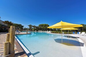 A clear blue swimming pool with a yellow umbrella, surrounded by lounge chairs and palm trees.