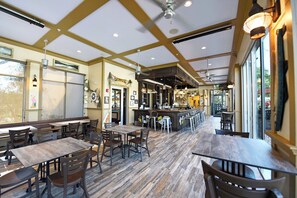 A restaurant with wooden tables and chairs, a bar area, and large windows.