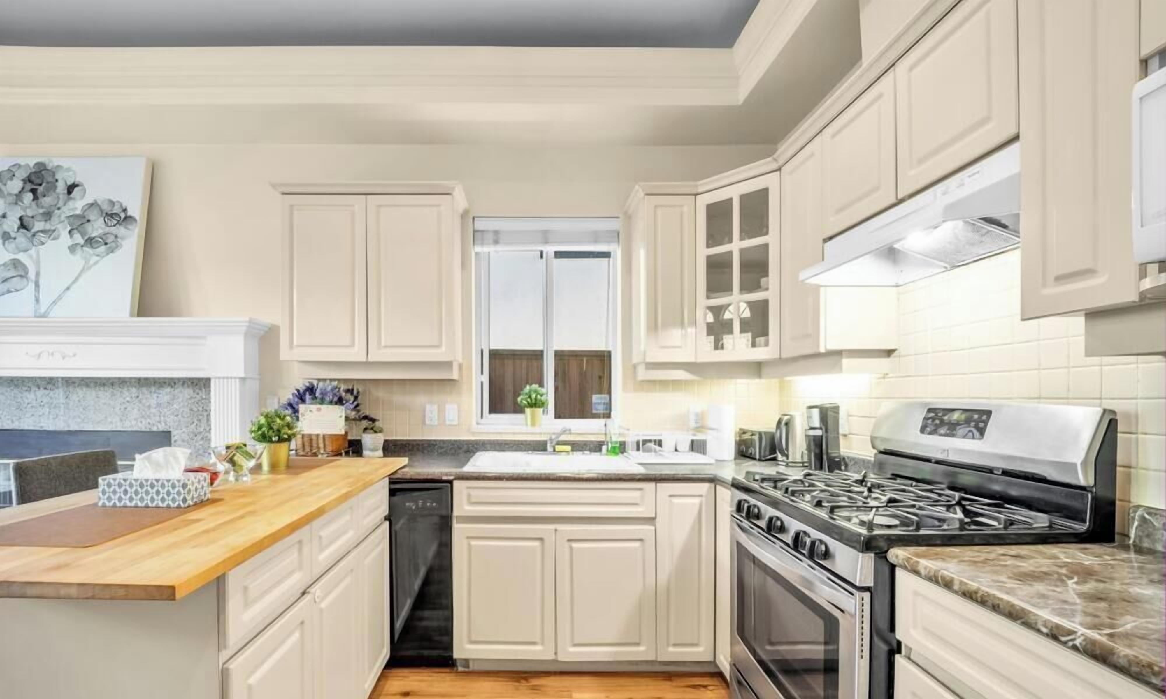 A modern kitchen with white cabinetry, a granite countertop, stainless steel appliances, and a window with a view.