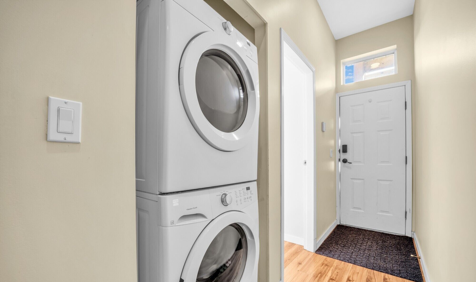 A laundry room with two stacked front-loading washing machines, a door, and a small window.