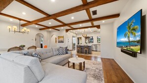 A modern living room with a sectional sofa, a round coffee table, and a large flat-screen TV mounted on the wall. - Oceanview Rooftop Escape, Modern Spanish Decor (San Diego)