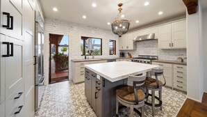 A modern kitchen with a large island, white cabinetry, and a chandelier. - Oceanview Rooftop Escape, Modern Spanish Decor (San Diego)