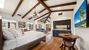 A spacious bedroom with a large bed, wooden beams, a dining area, and a kitchen with dark cabinets. - Oceanview Rooftop Escape, Modern Spanish Decor (San Diego)