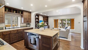 A spacious kitchen with wooden cabinets, a central island, and a dining area with a sofa. - Majestic Corner Coastal Haven (San Diego)