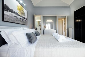 A neatly made bed with white and gray bedding, a large framed picture on the wall, and a view into the bathroom. - CASA  BILA (Chania)