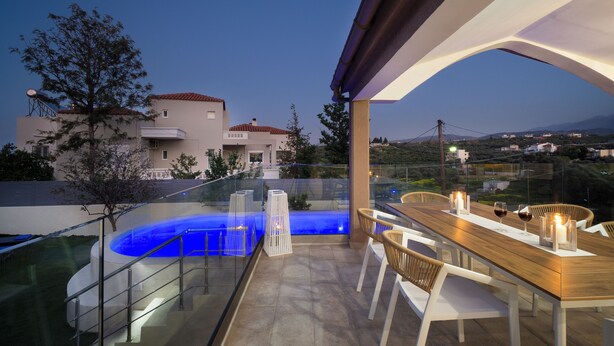 Uma área moderna de refeições ao ar livre com piscina, guarda-corpos de vidro e vista para a paisagem circundante.