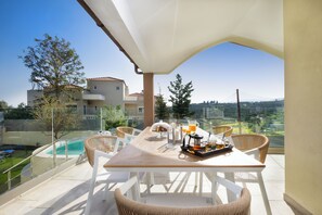 A balcony with a table set for breakfast, overlooking a swimming pool and a residential area. - CASA  BILA (Chania)