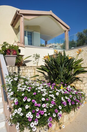 A modern house with a covered patio, a stone wall, and a variety of flowers. - CASA  BILA (Chania)
