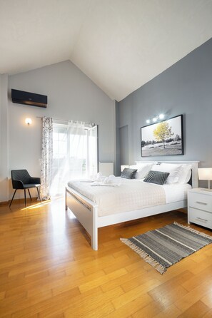 Een slaapkamer met een bed, een stoel, een nachtkastje, een raam met gordijnen en een schilderij aan de muur.