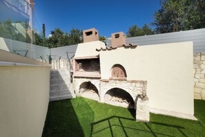 A patio area with a stone fireplace, a small wooden structure, and a staircase leading up to a balcony. - CASA  BILA (Chania)