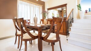 Uma área de refeições com uma mesa e cadeiras de madeira, um candelabro e uma escada que dá para um andar superior.