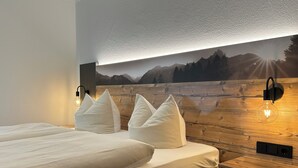 Een hotelkamer met een houten hoofdeinde, een groot bed met witte beddengoed en een wandlamp.