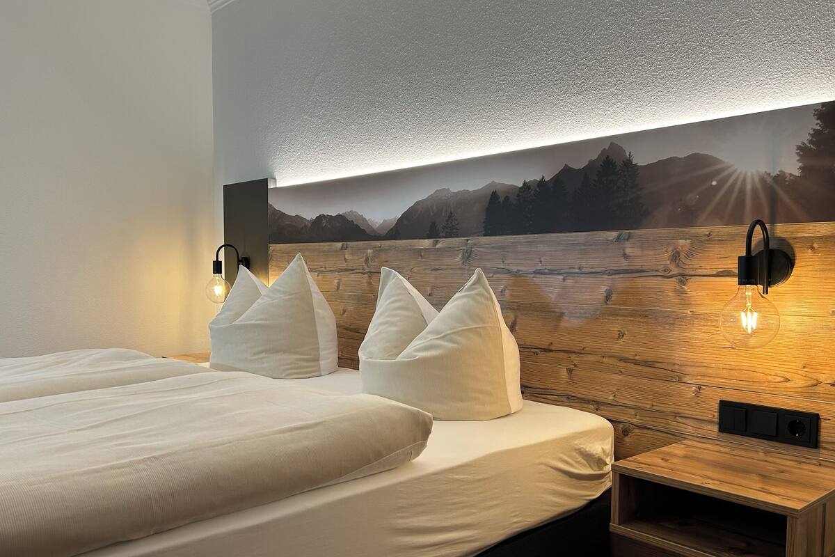 Een hotelkamer met een houten hoofdeinde, een groot bed met witte beddengoed en een wandlamp.