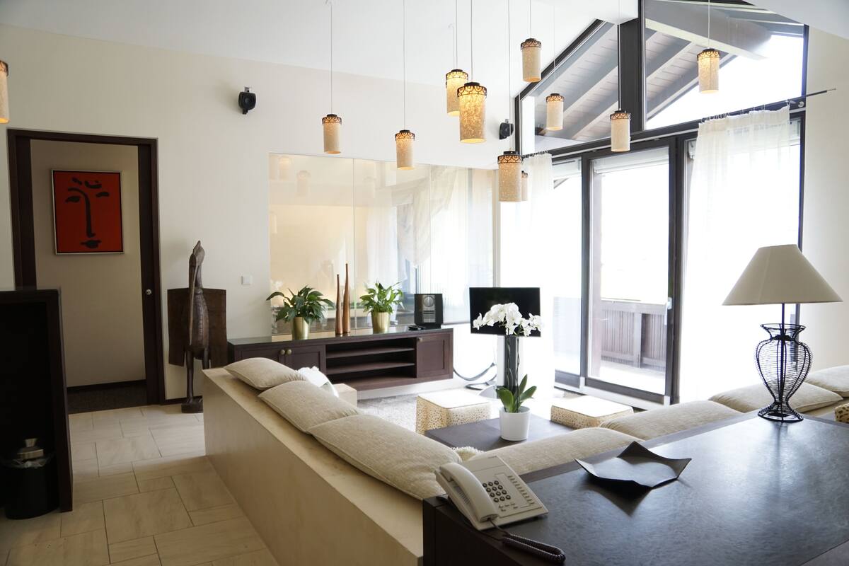 Een moderne woonkamer met een bank, een salontafel, een televisie en een groot raam met gordijnen.
