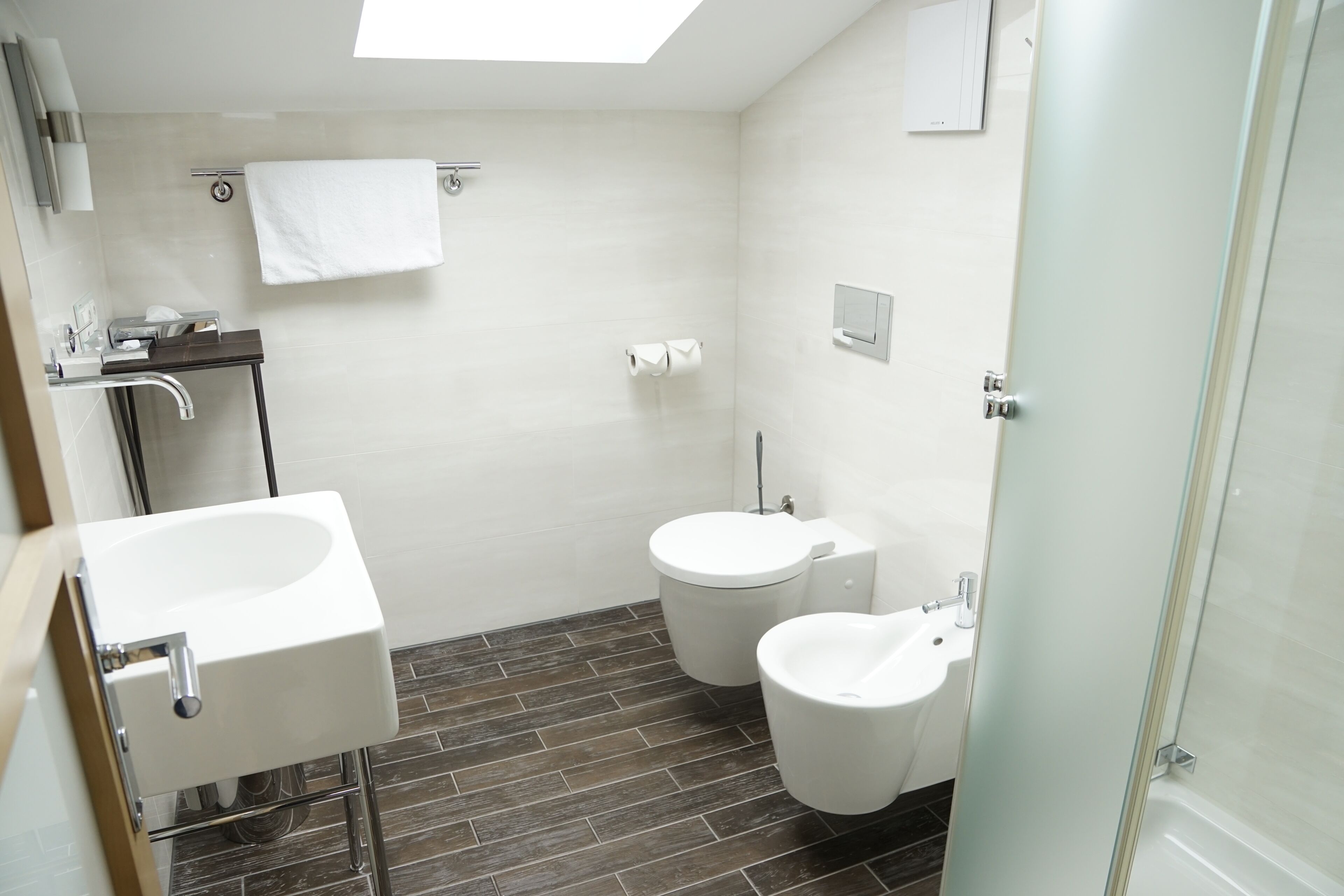 Een moderne badkamer met een douche, een wastafel, twee toiletten en een glazen deur.